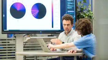 Two people pointing at a computer 