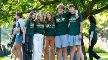 5 students wearing green and gold shirts smiling at the camera with arms around each other