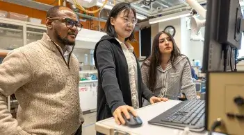 Two graduate students collaborate with their professor in a research lab