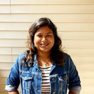 A smiling student, outdoors, standing next to a yellow-beige structure