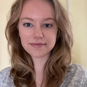 Headshot of a smiling Samantha in front of a yellow-beige background