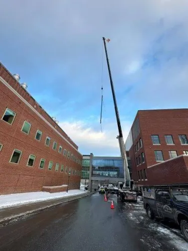 Overhead crane lifting large pipe above Stafford building 