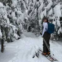 Lucy Krokenberger on skis, looking back at the camera in a snowy forest