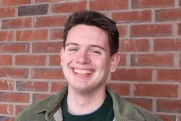 Person smiling in front of a brick wall.