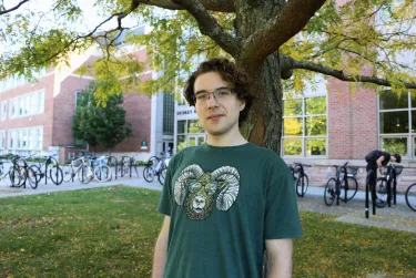 Person standing under a tree near a building with parked bicycles.