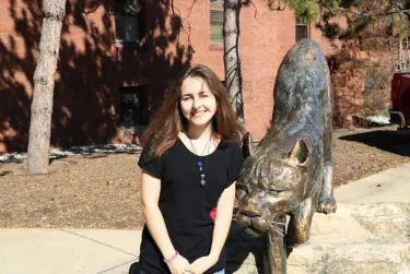 Person smiling outdoors beside a bronze statue.