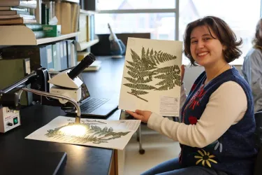 a young woman holding up a pressed plant specimen in a lab