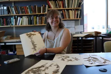 a young woman holding up a pressed plant specimen in a lab