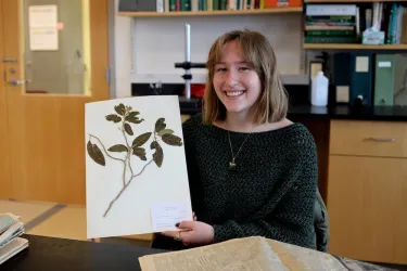 a young woman holding up a pressed plant specimen in a lab