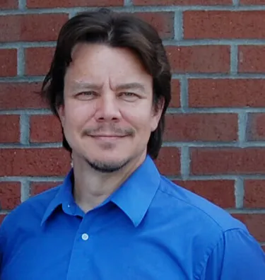 A person wearing a blue shirt standing in front of a brick wall