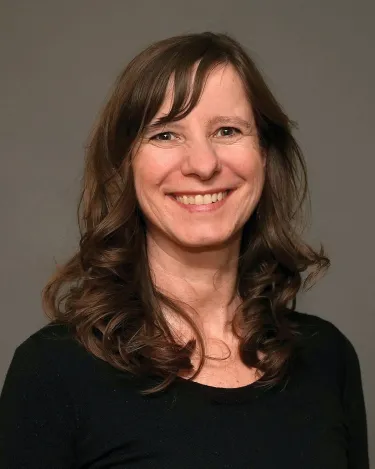 A person with long hair wearing a black shirt and a white coat
