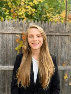 A person wearing blazer standing in front of trees