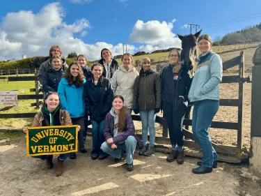 UVM students posing with a UVM flag in front of a horse pasture in Ireland
