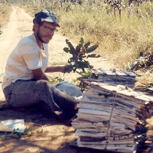 A young Dr. Hill sits by a dirt road, pressing stacks of specimens in newspaper