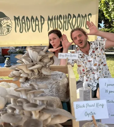 Two people at a farm stand selling mushroom having fun