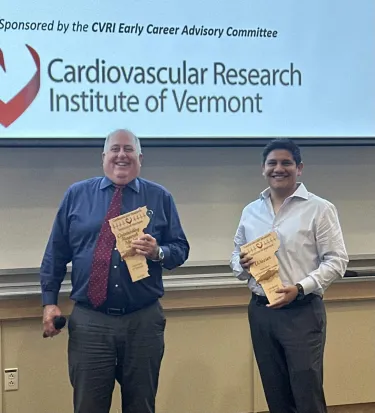 2 Men standing in front of a screen holding awards shaped like Vermont