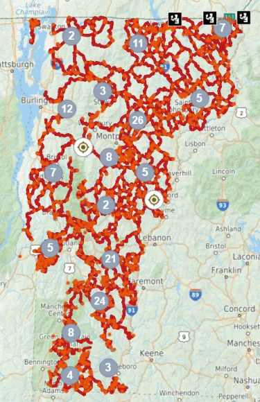 Map showing a network of interconnected trails across Vermont and surrounding areas, with clusters marked by blue circles containing numbers indicating trail counts. Key markers include black icons in the northeast and beige compass symbols, highlighting trail density and navigation points.