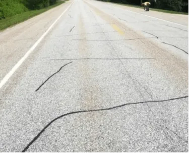 A photograph of a road with multiple thin cracks running perpendicular to the road due to temperature variability
