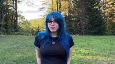 Portrait of a student standing in a grassy clearing surrounded by trees.
