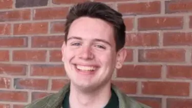 Smiling person in front of a red brick wall.