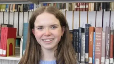 Student standing in front of library bookshelves.