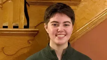 Student standing indoors near a wooden staircase.