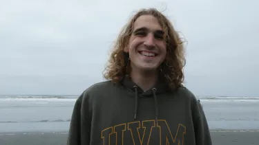 Portrait of a student standing on a beach, with ocean waves and an overcast sky in the background.