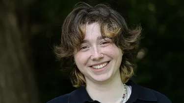 Portrait of a student outdoors with trees and greenery in the background.