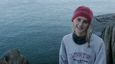Portrait of a student standing on a rocky shoreline beside a large body of water.