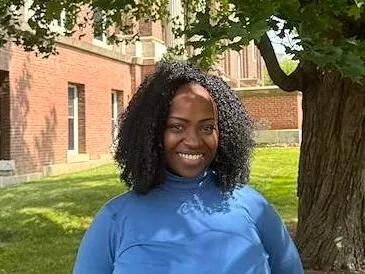 Person in a blue top smiling beside a tree.