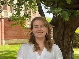 Person smiling outdoors beside a tree.