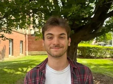 Person smiling outdoors in front of a tree.
