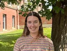 Person smiling outdoors beside a tree.