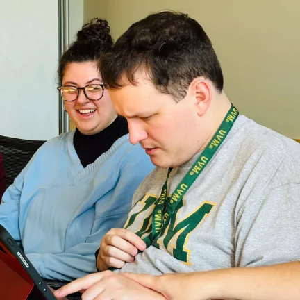 A college student works on an assistive communication device as a communication support person looks on