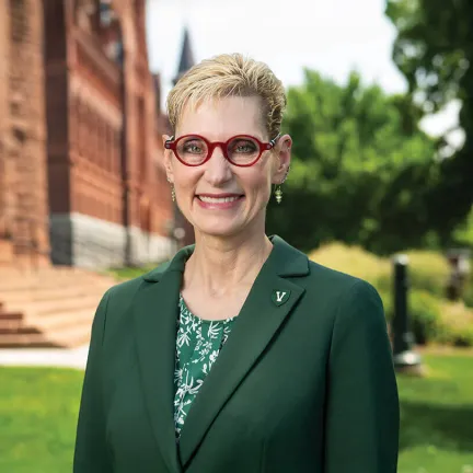 The president, dressed in green, smiles in front of a classic brick building.