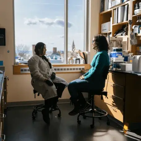 Two people sitting in a lab, facing each other with a window in the background