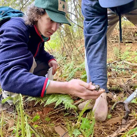 two students inspect a soil sample in the forest