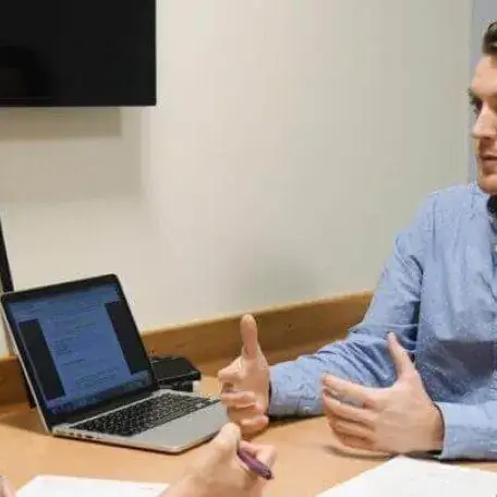 Two people sitting across from each other at a desk with laptops