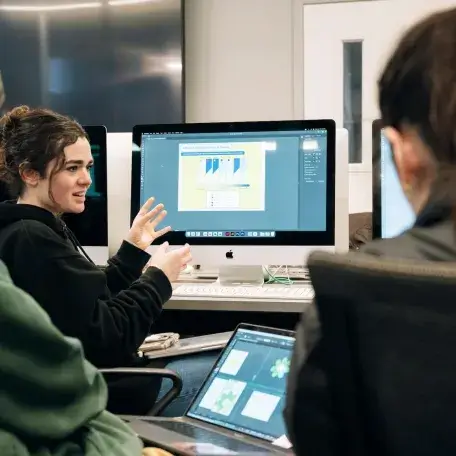 Students discussing communication design projects in a computer lab