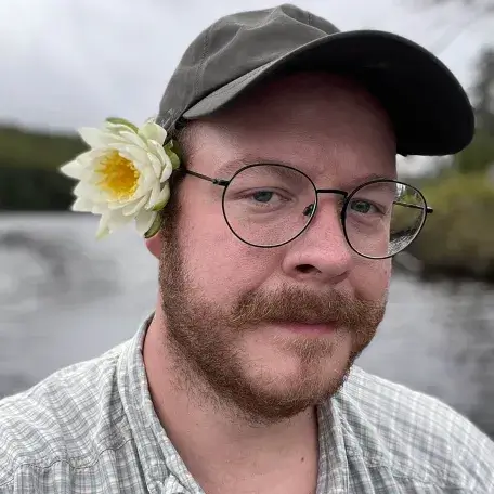 Andrew May outdoors with a cap on and a flower behind his ear