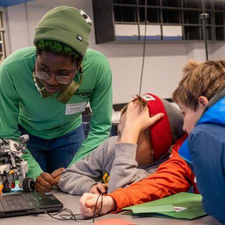 a college student helps two youngsters with a science project