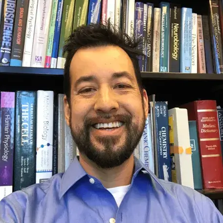 Jom, with a full face smile, in an office setting with book lined shelves in the background