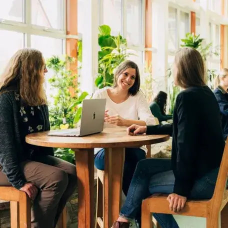 A group of three faculty members sitting at a round table talking and smiling