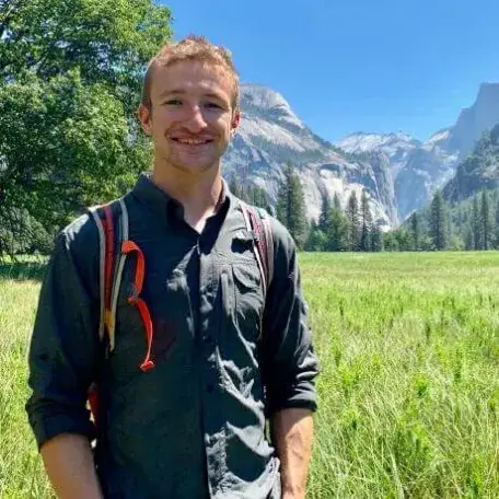 Soren standing in a grassy field with mountains and pine trees in the background