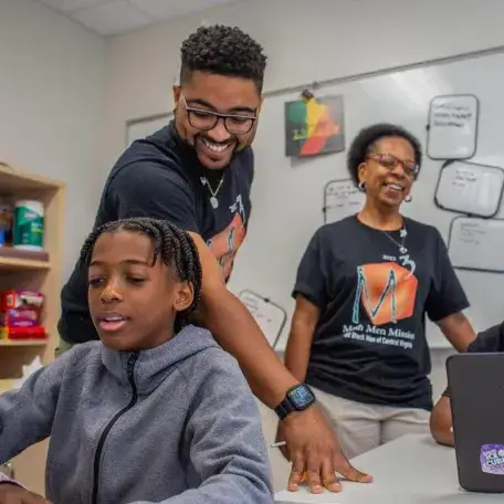 Daniel Fairley G'16 smiles and he works with students in a classroom.