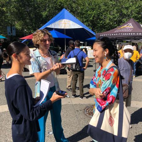 Two student reporters interview a Farmer's Market patron on a sunny day.