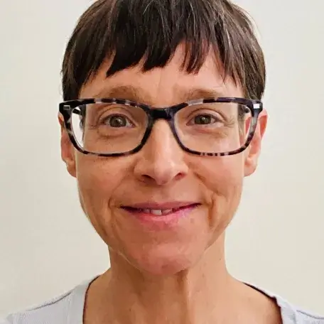Freda standing in front of a white backdrop, smiling and wearing glasses.