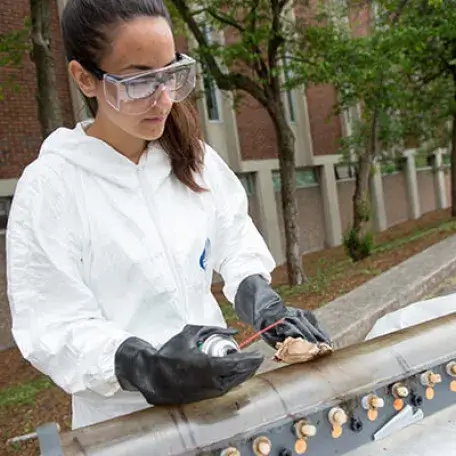 ME student cleaning research device outside of Votey Hall