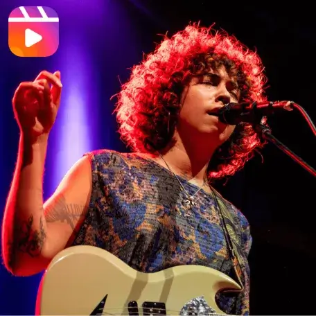 Person singing on stage with a microphone and guitar