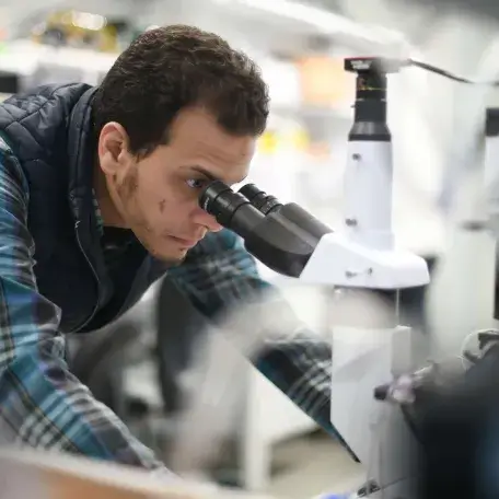 Scientist looking into a microscope in a lab, links to Past Research Projects Page 